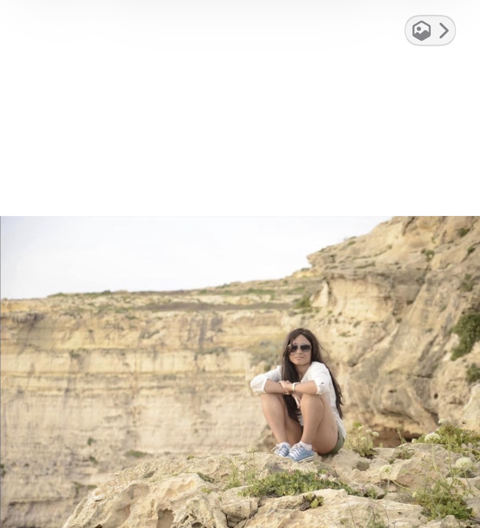 Cass in aviators and a white shirt, sitting on the cliff edge of the Azure Window on Gozo, Malta.