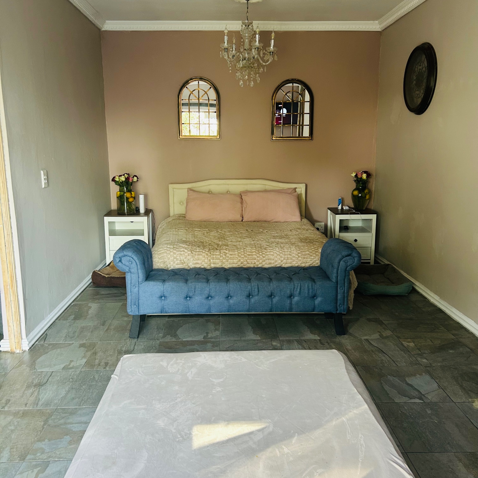 Pink and taupe bedroom with tufted blue chaise, arched gold mirrors and crystal chandelier
