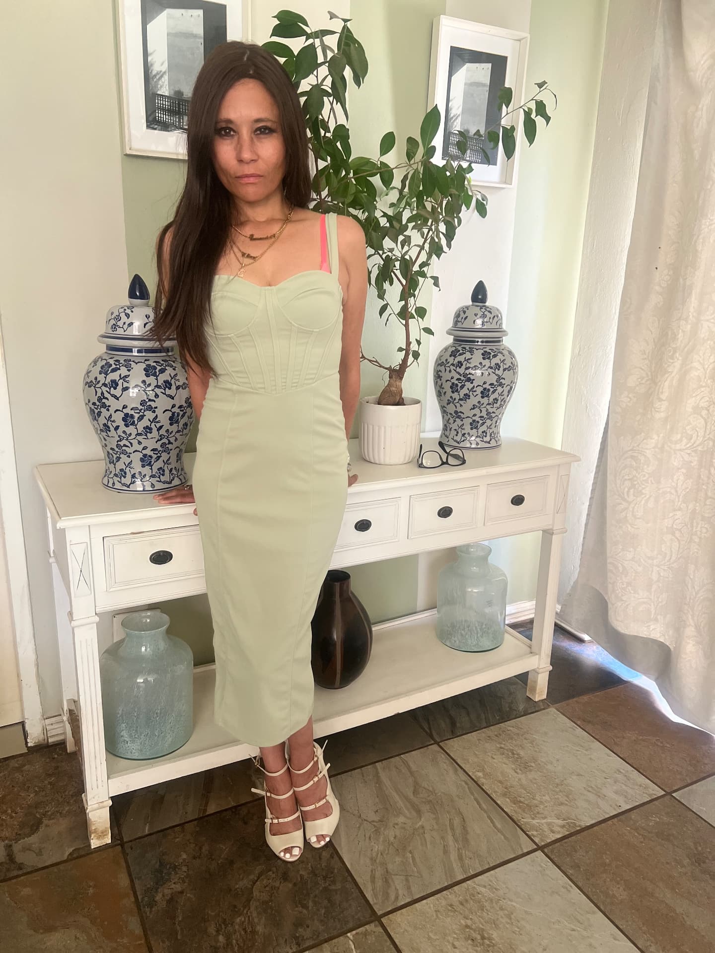 Cass in a powder-mint corset midi dress with nude studded strappy sandals, beside a cream console table