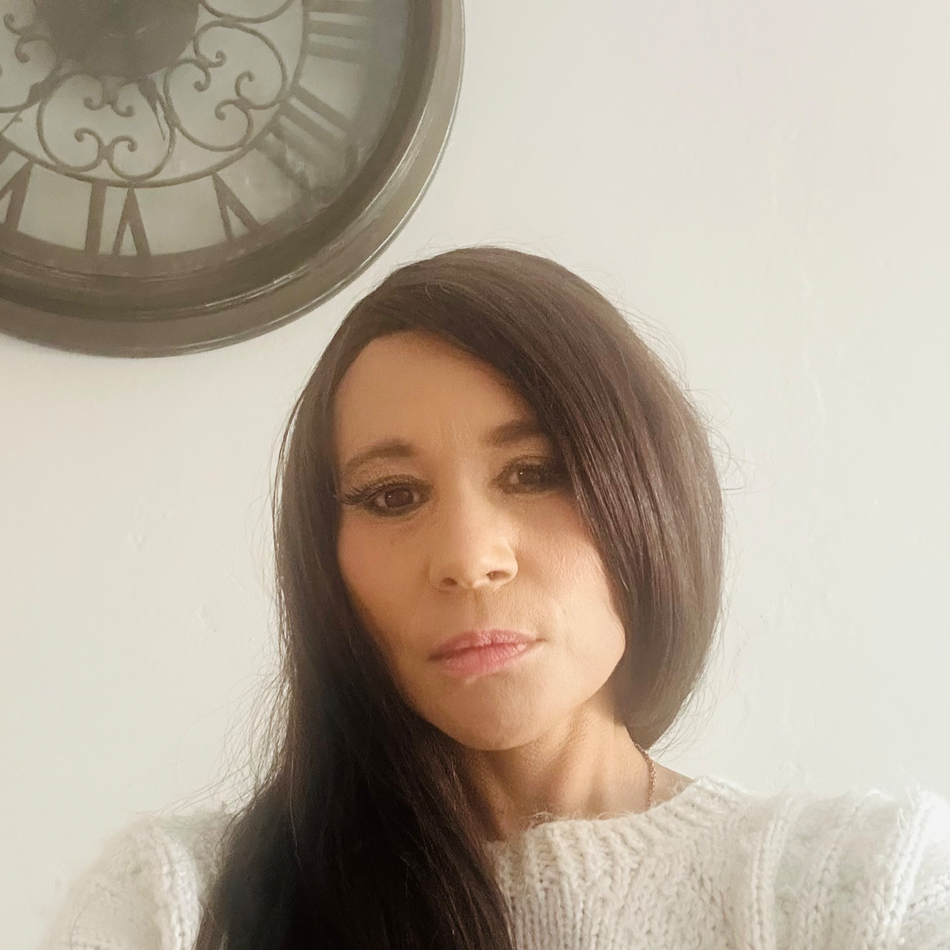 Portrait of Cass with softly contoured makeup beneath a large wall clock