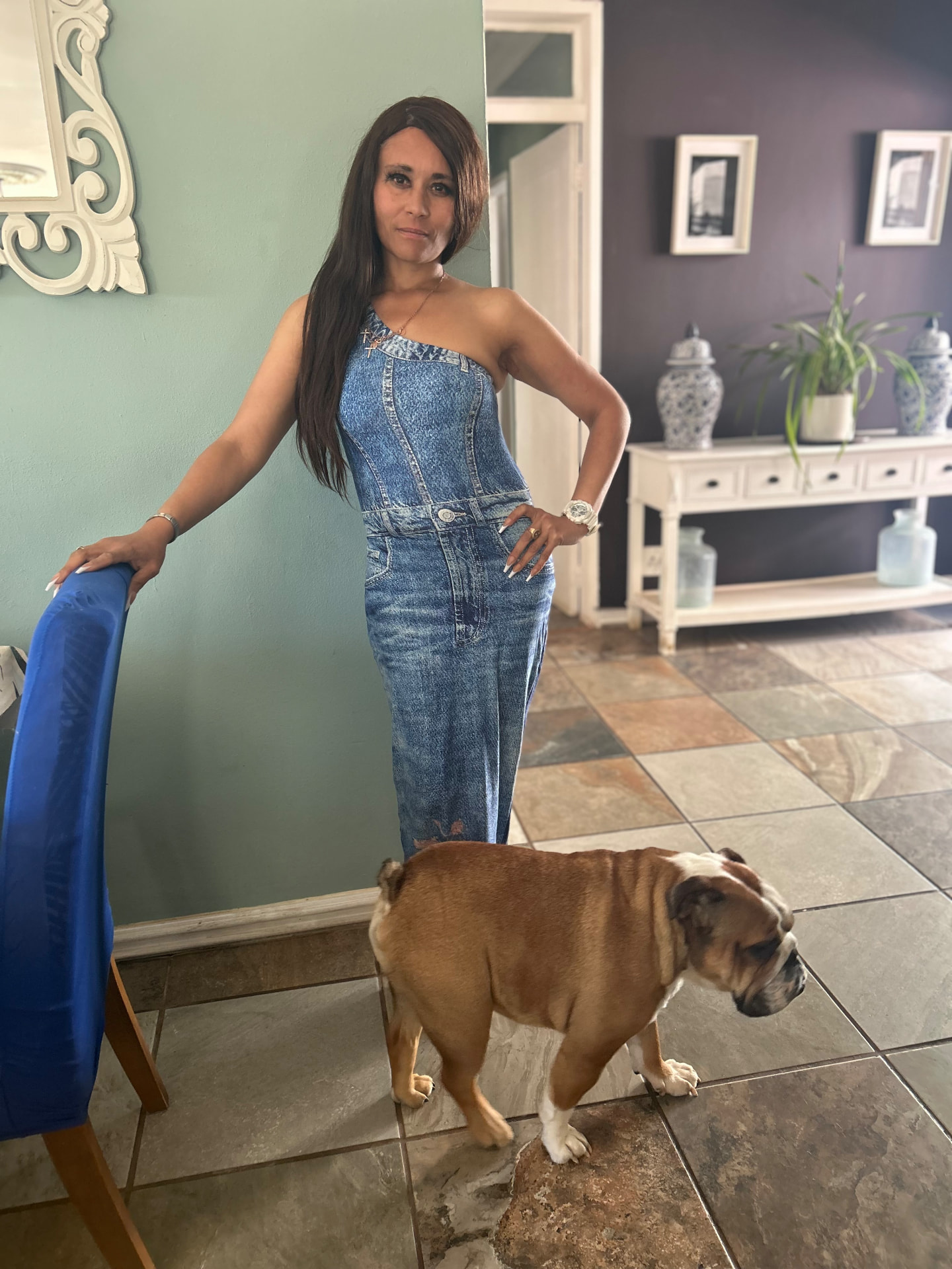 Cass in the denim maxi jumpsuit with a gold watch, her bulldog Stretford walking past