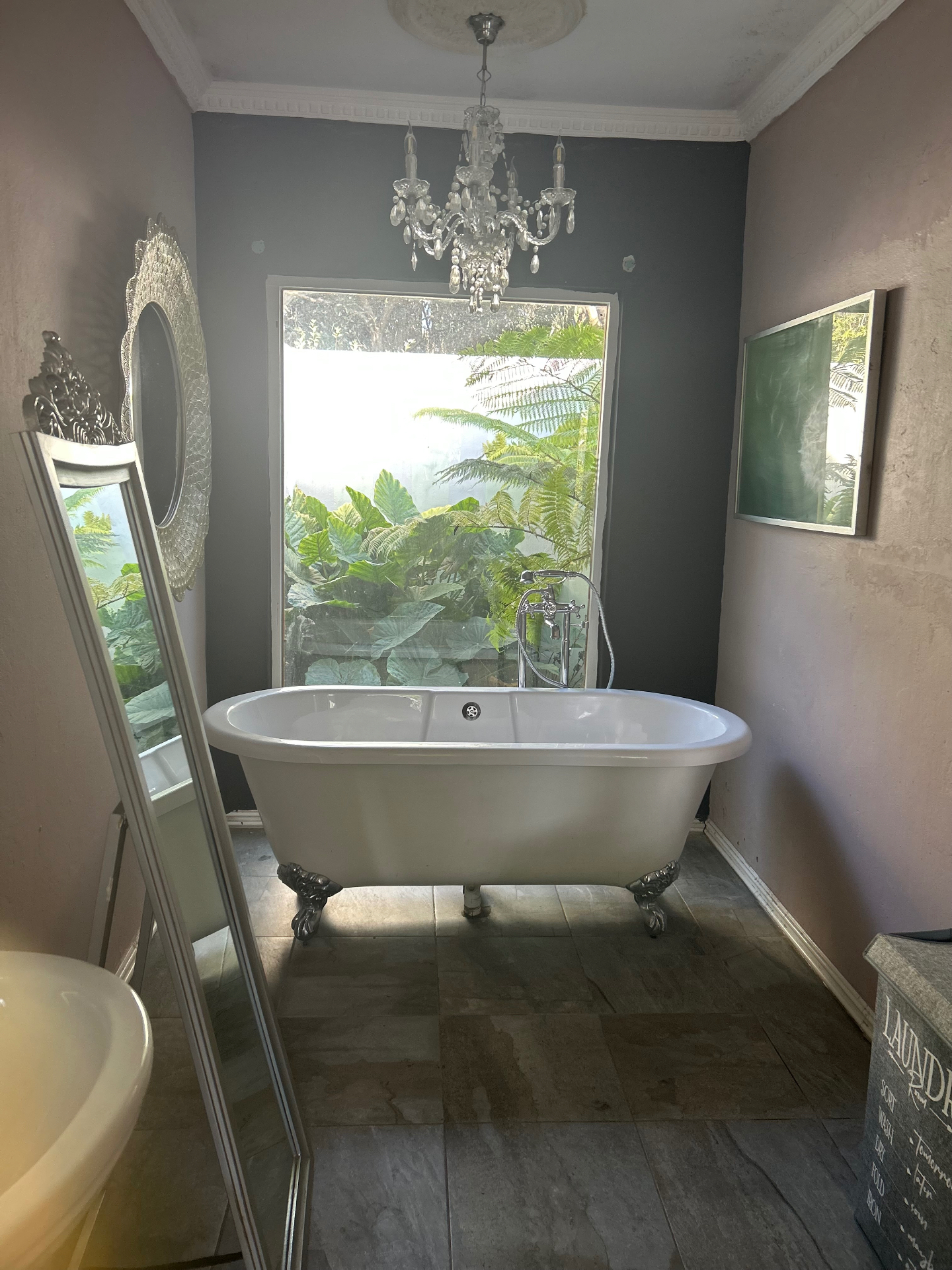 Freestanding claw-foot bath under a crystal chandelier with a jungle view