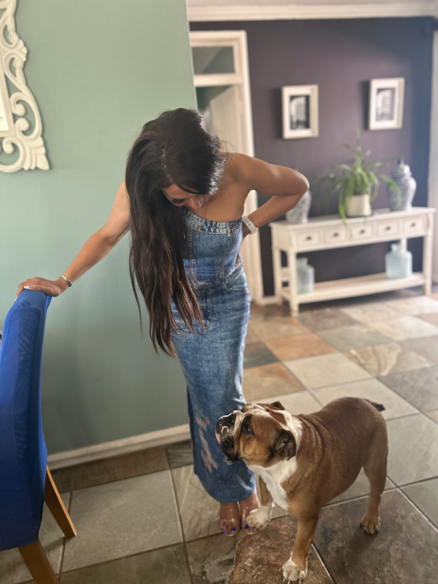Cass bending to look at her English bulldog Stretford, who poses for the camera, while she wears a denim maxi jumpsuit
