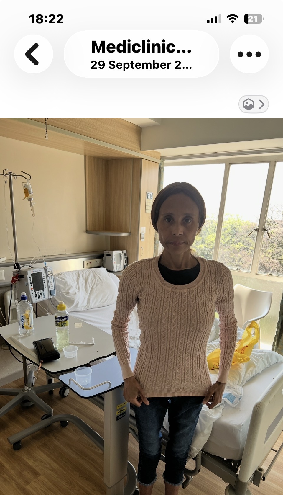 Cass standing in her hospital room in a cream cable-knit jumper and jeans, painfully thin, on the day she was discharged