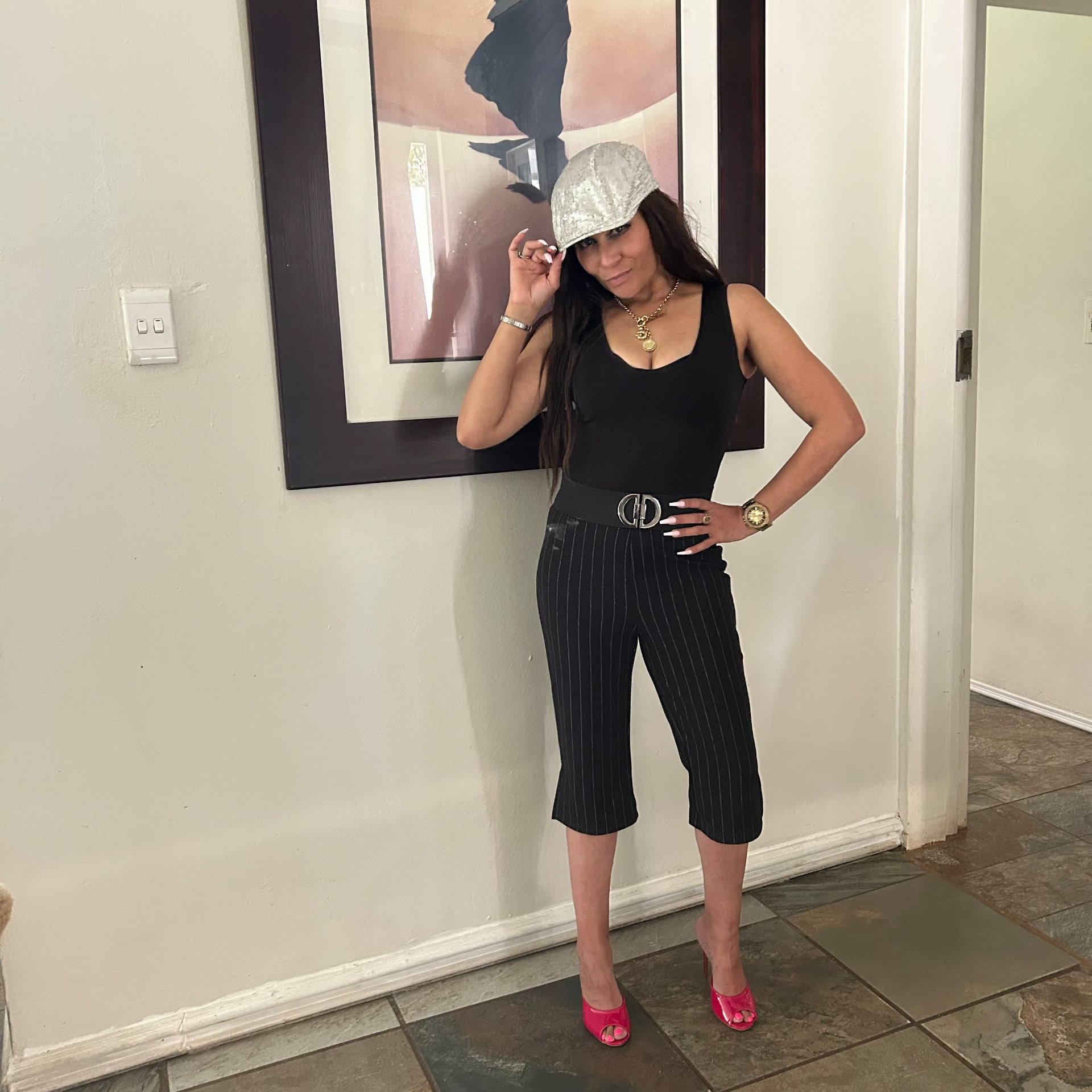 Cass tipping a silver sequinned baker-boy cap in a black bodysuit, black pinstripe capri pants and pink mule heels