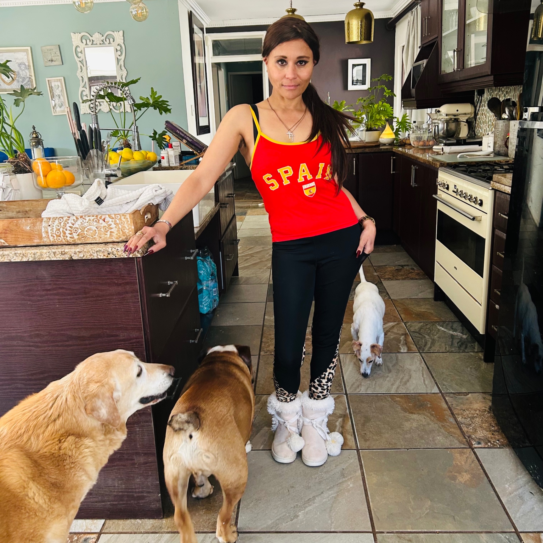Cass in a red España vest, black leopard-panel leggings and pom-pom fur boots, celebrating in her kitchen with her dogs around her