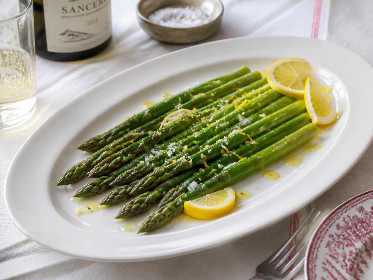 Blanched green asparagus on a white platter with lemon zest and melted butter