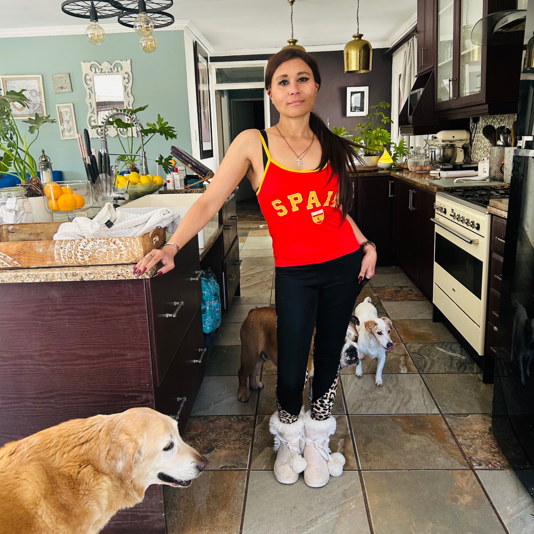 Cass smiling softly in her red España vest, hand on the kitchen island