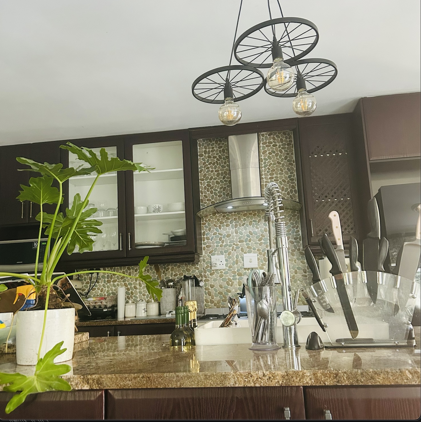Industrial wheel chandelier above a dark kitchen with pebble mosaic backsplash