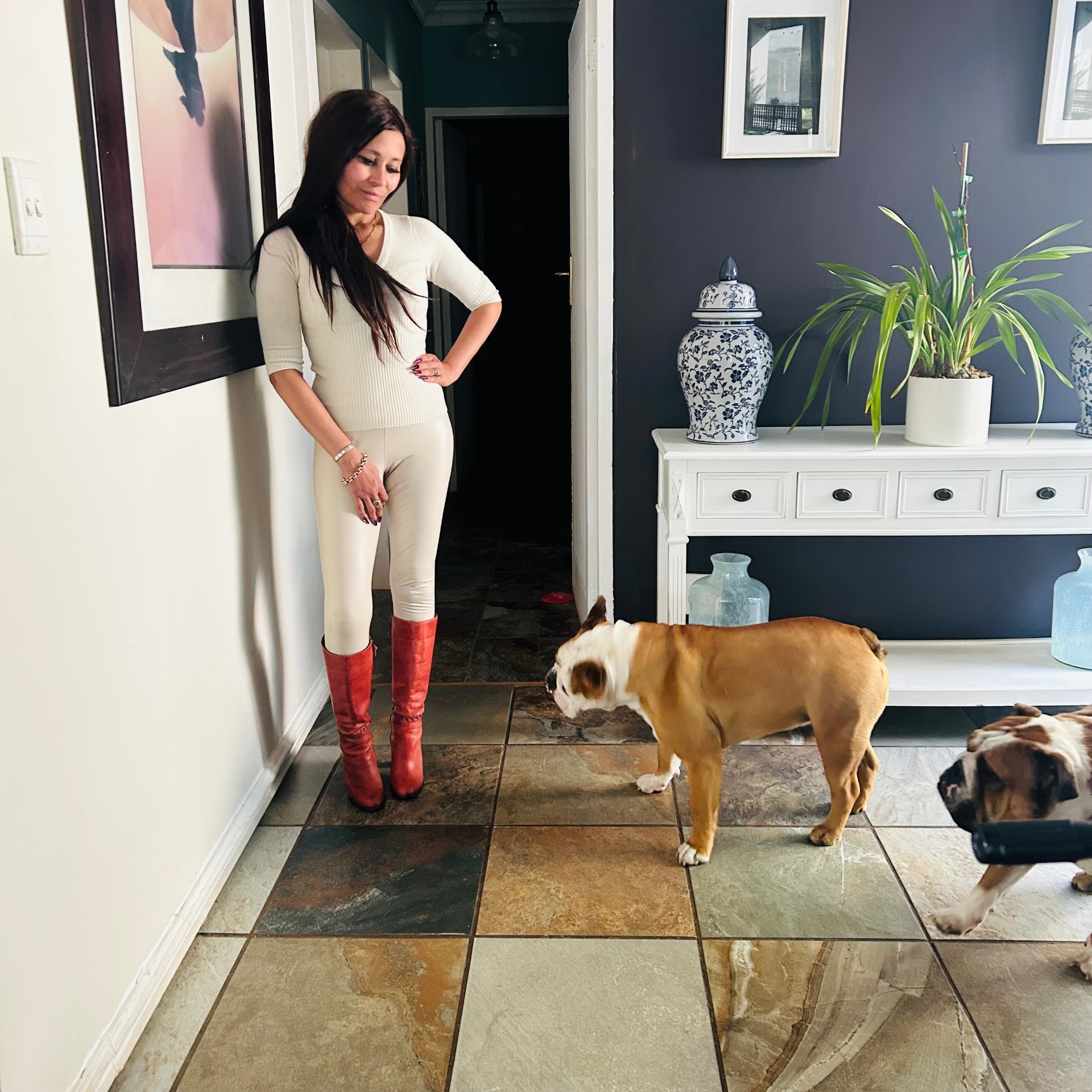 Cass smiling down at Churchill the English bulldog in the hallway, wearing cream leggings and red Socrati boots