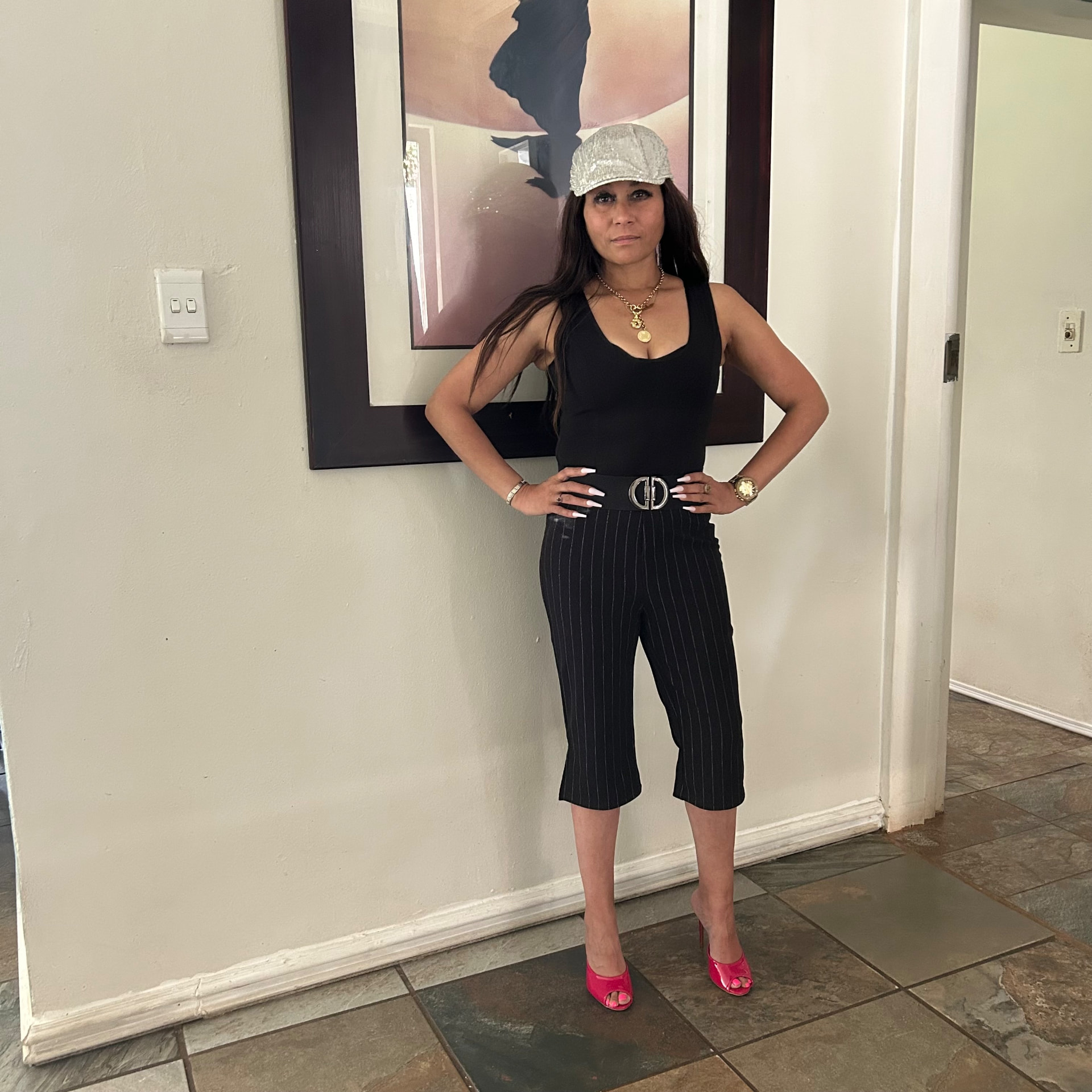 Cass standing with hands on hips in the black bodysuit, pinstripe capris, sequinned cap and pink heels