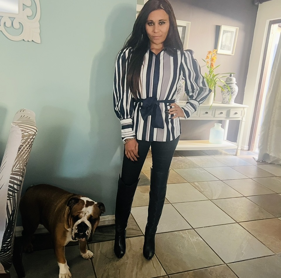 Cass in a navy and white striped bow-tie blouse, black skinny jeans and knee-high leather boots, with her bulldog beside her