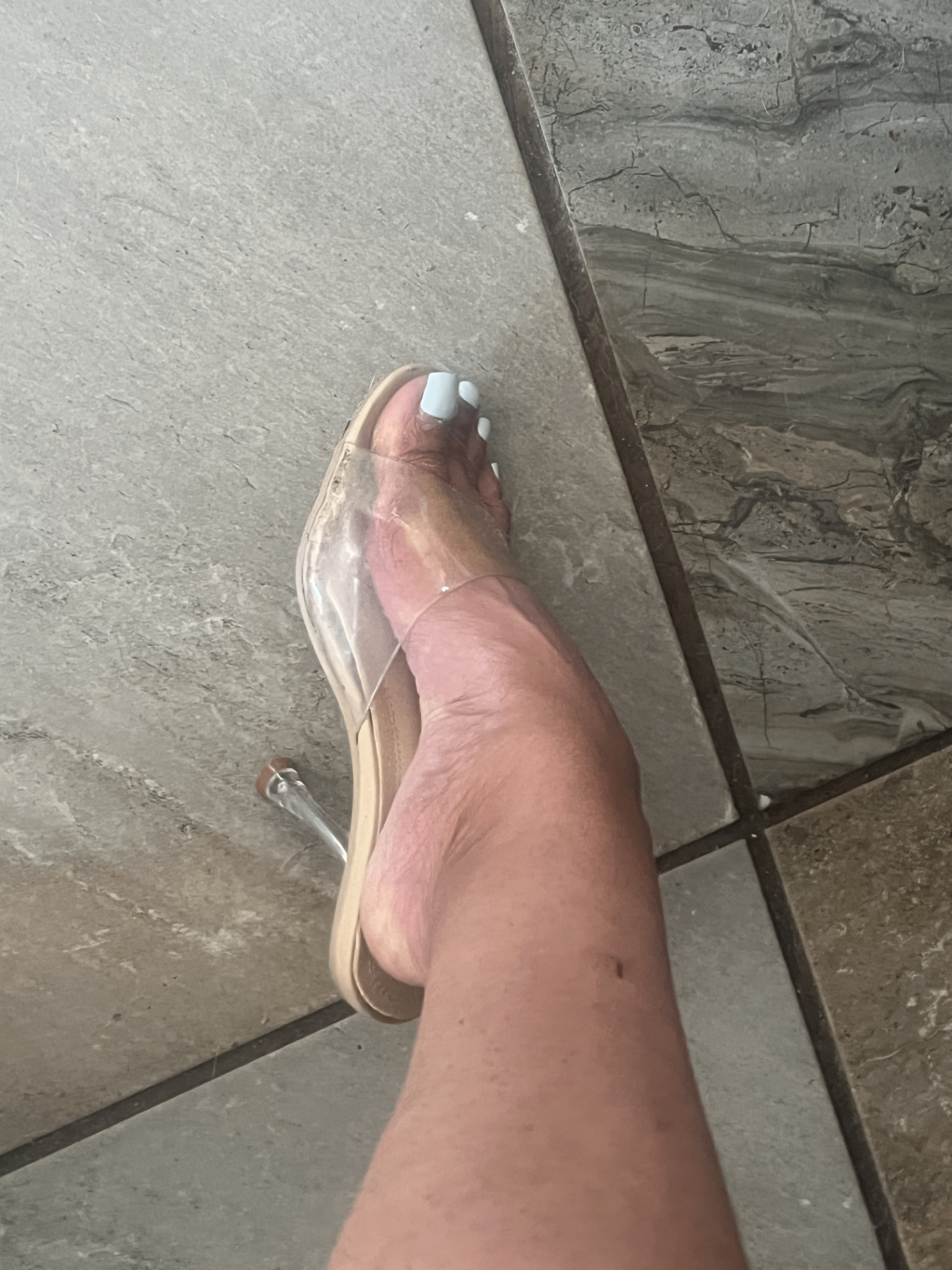 Cass's foot in a clear heeled mule, visibly in spasm — the tendon pulled taut, the arch cramped