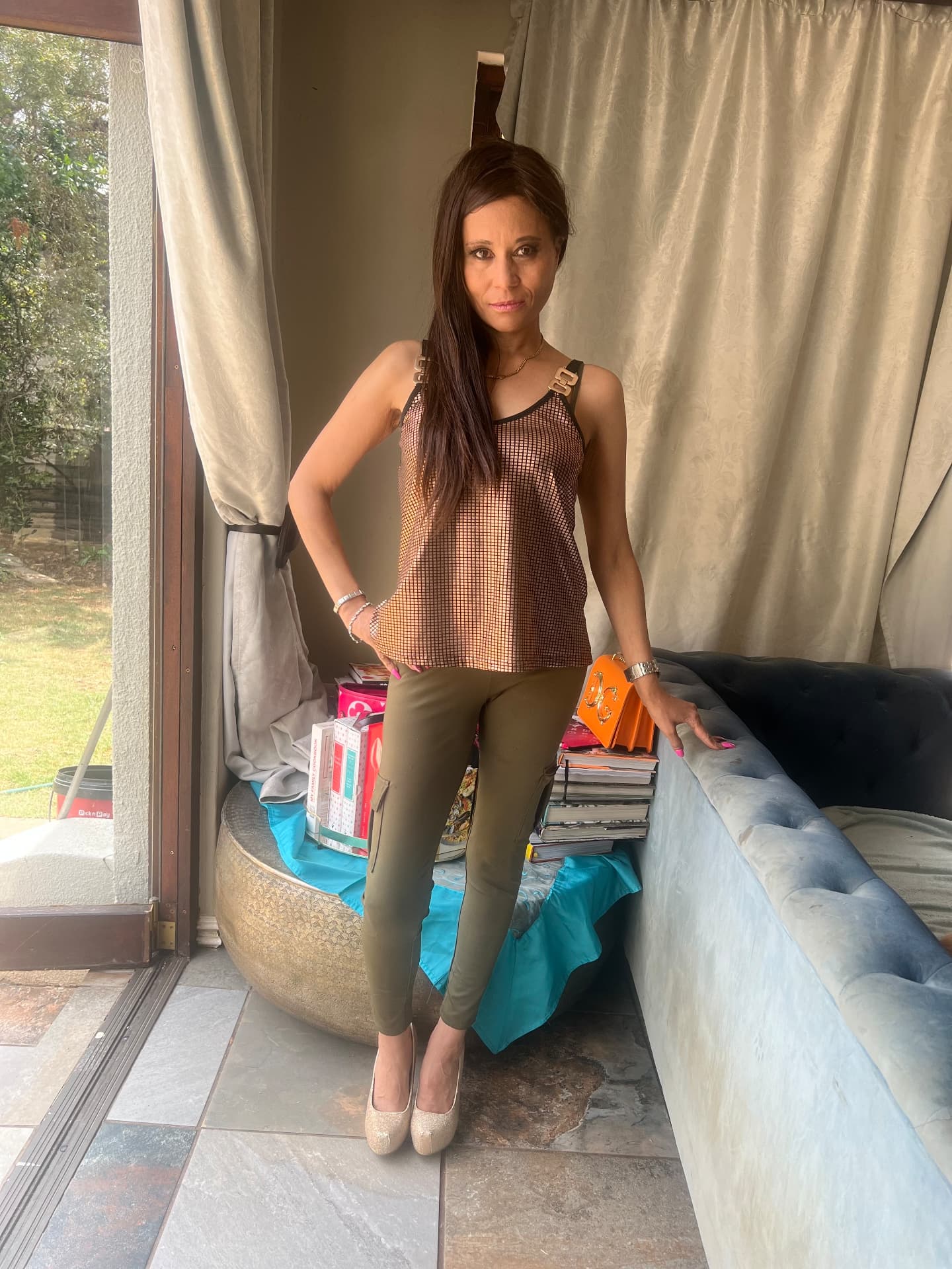 Cass in khaki cargo trousers, a gold chainmail top, gold glitter heels and an orange bag — her SA supporter uniform