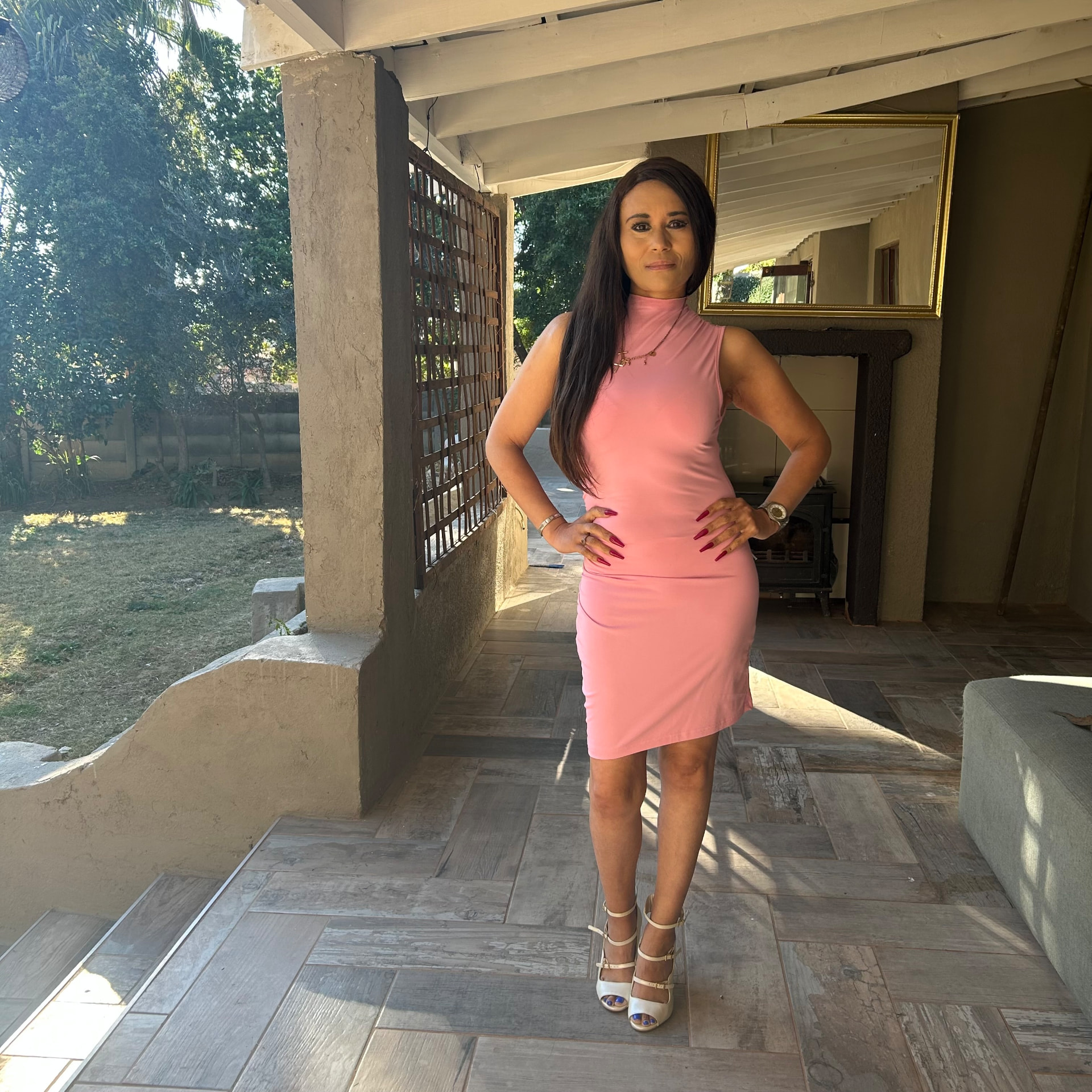 Cass in a sleeveless pink ruched dress and white Brazilian heels on her renovated patio