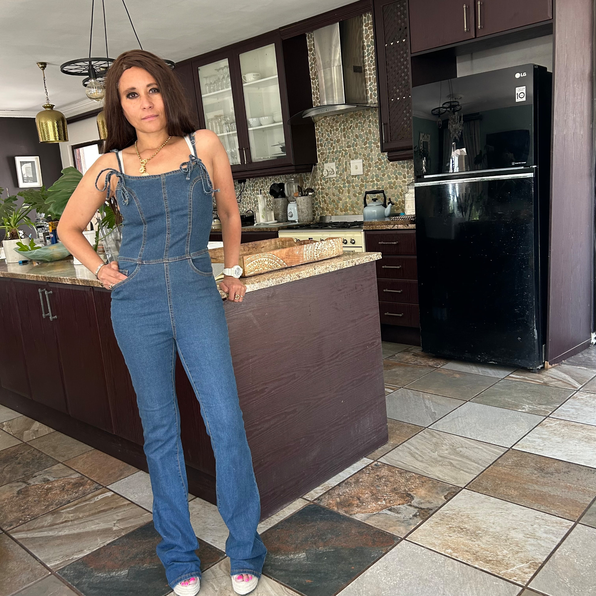 Cass in her denim jumpsuit with tie-strap shoulders and espadrille wedges, standing in the kitchen