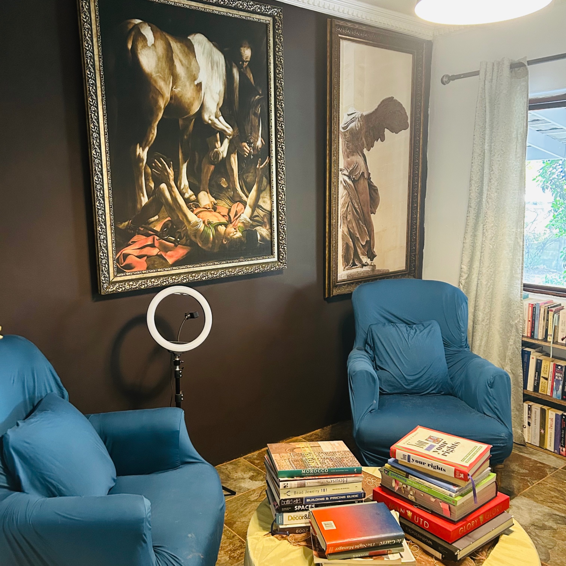 Reading room with Caravaggio Conversion of Saul, Winged Victory print and blue armchairs