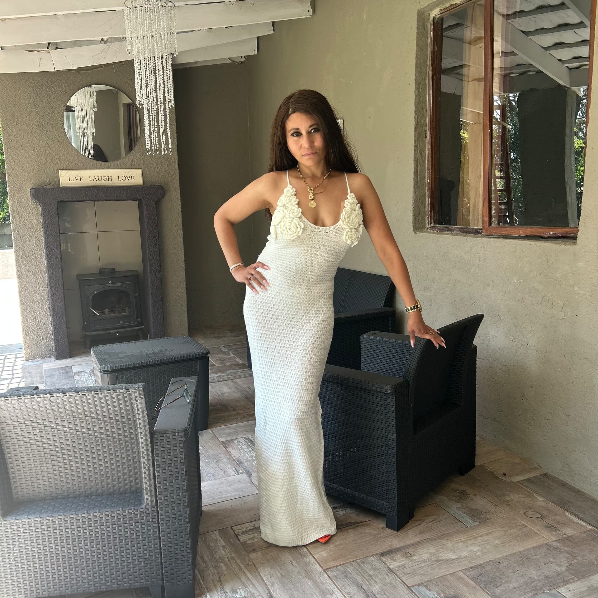 Side view of Cass in the ivory crochet maxi dress with rose appliqués on the straps, on the patio