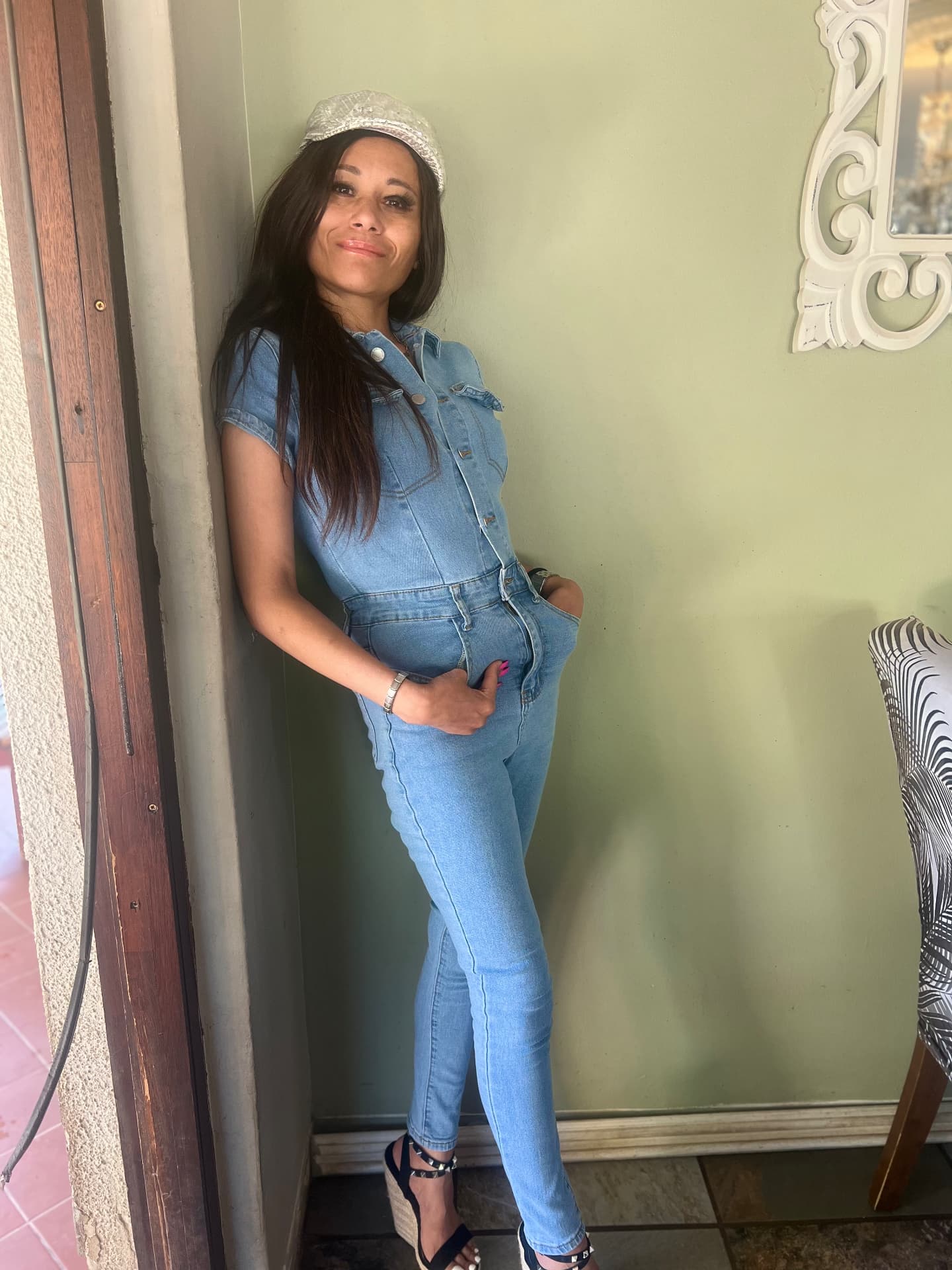 Cass in September 2025 in the same denim jumpsuit with a cream baker boy cap and studded wedges