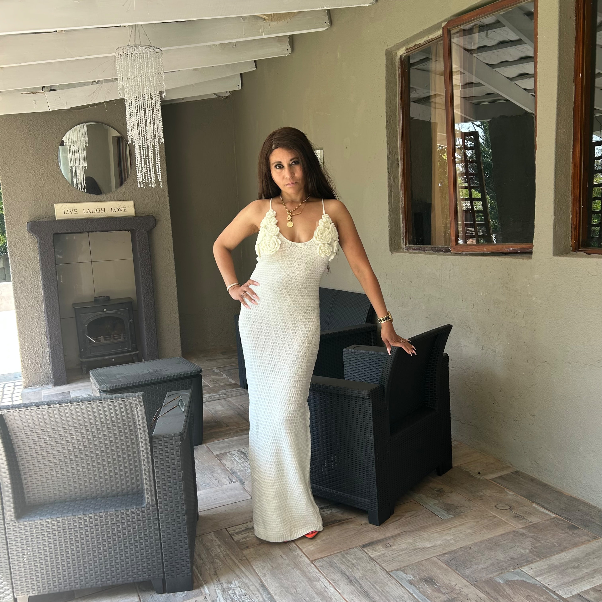 Cass in the cream crochet maxi dress and gold necklace near the round mirror and crystal chandelier on the patio