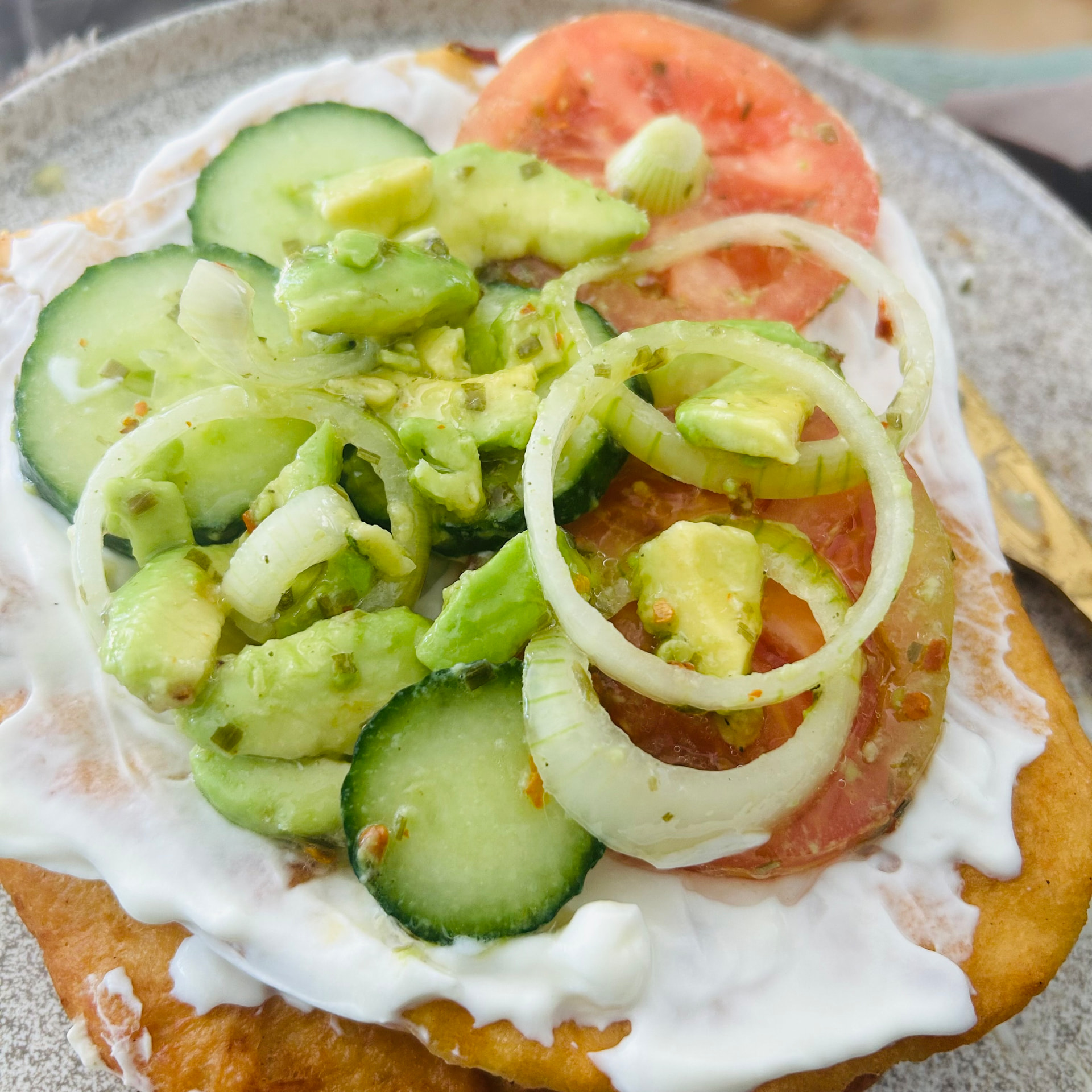 Lemony labneh on lángos with avocado, cucumber, tomato and onion rings