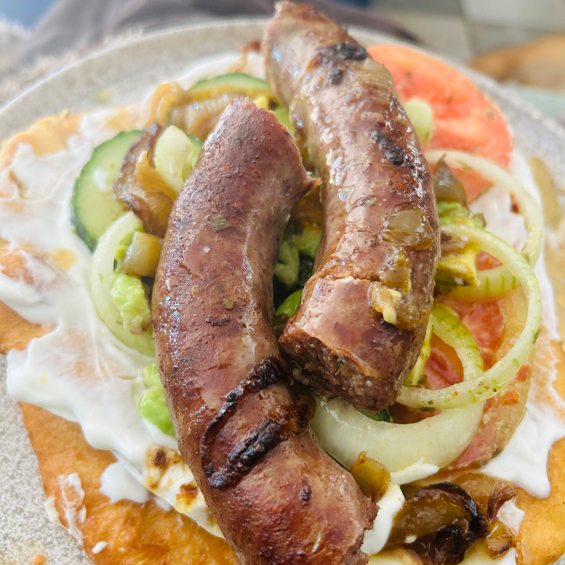 Two browned boerewors on a lángos with labneh and salad