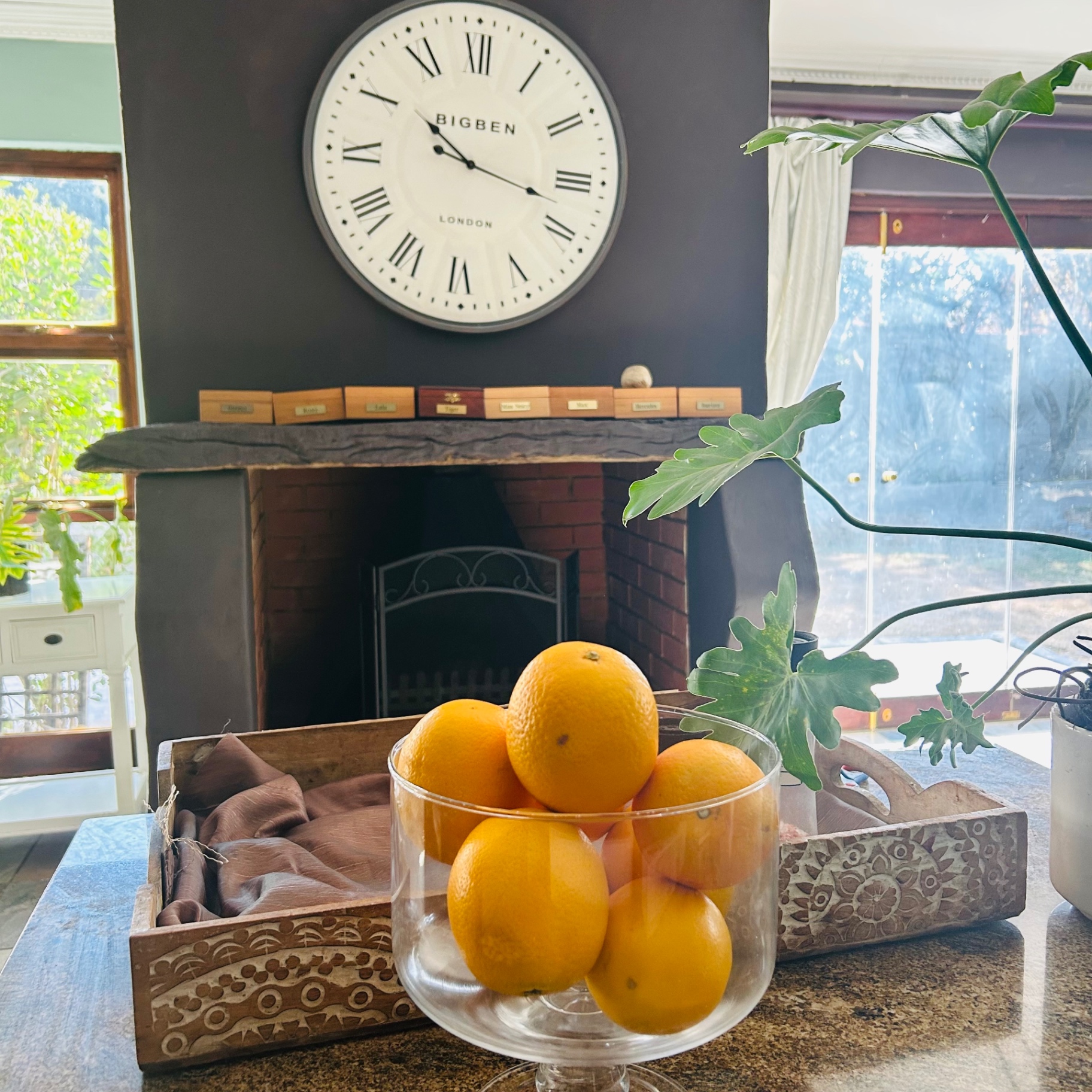 Bowl of oranges on granite island with carved wooden tray, Big Ben clock and inky fireplace behind