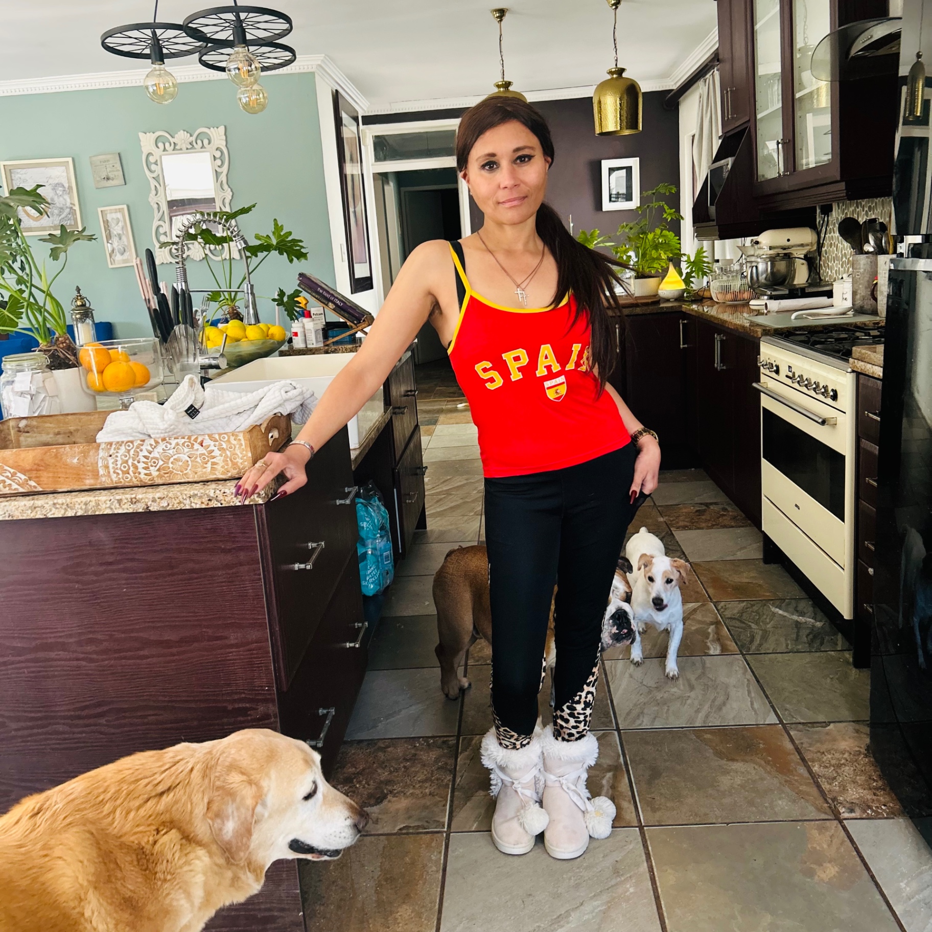 Cass in her kitchen in a red Spain vest with the whole pack of dogs around her, sun through the windows