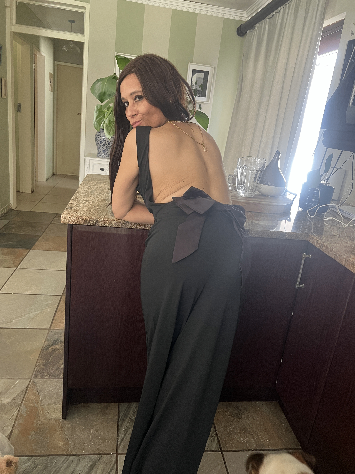 Back view of Cass in a fully backless black jumpsuit garnished with an oversized bow at the waist