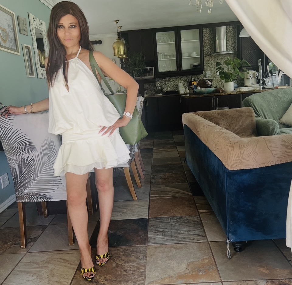 Cass in a white halter-neck ruffled mini dress with yellow and black zebra-print heels, carrying a large olive-green Michael Kors tote
