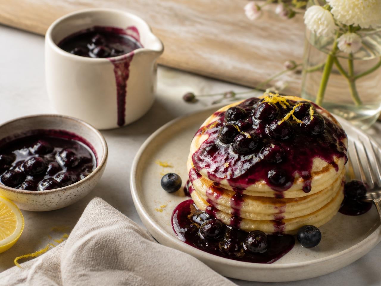 Warm blueberry compote in a jug and bowl, spooned over pancakes