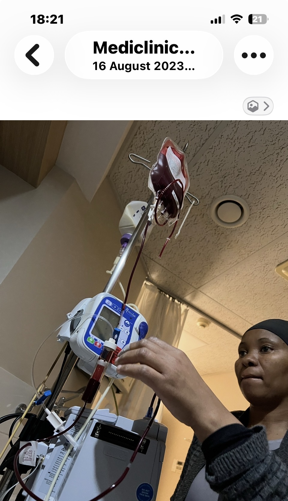 A nurse setting up an IV pump with a bag of red blood cells hanging on the drip stand above Cass's hospital bed