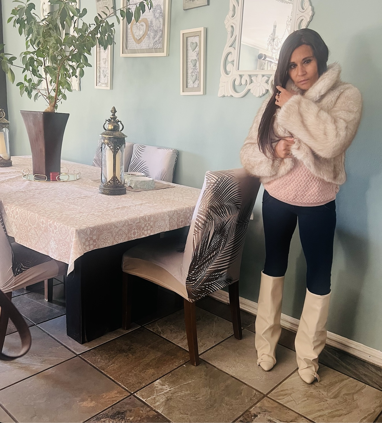 Cass in a cream faux fur jacket over a baby pink cable-knit jumper, dark Freddie jeans and cream wedge knee boots, in a soft blue-green dining room