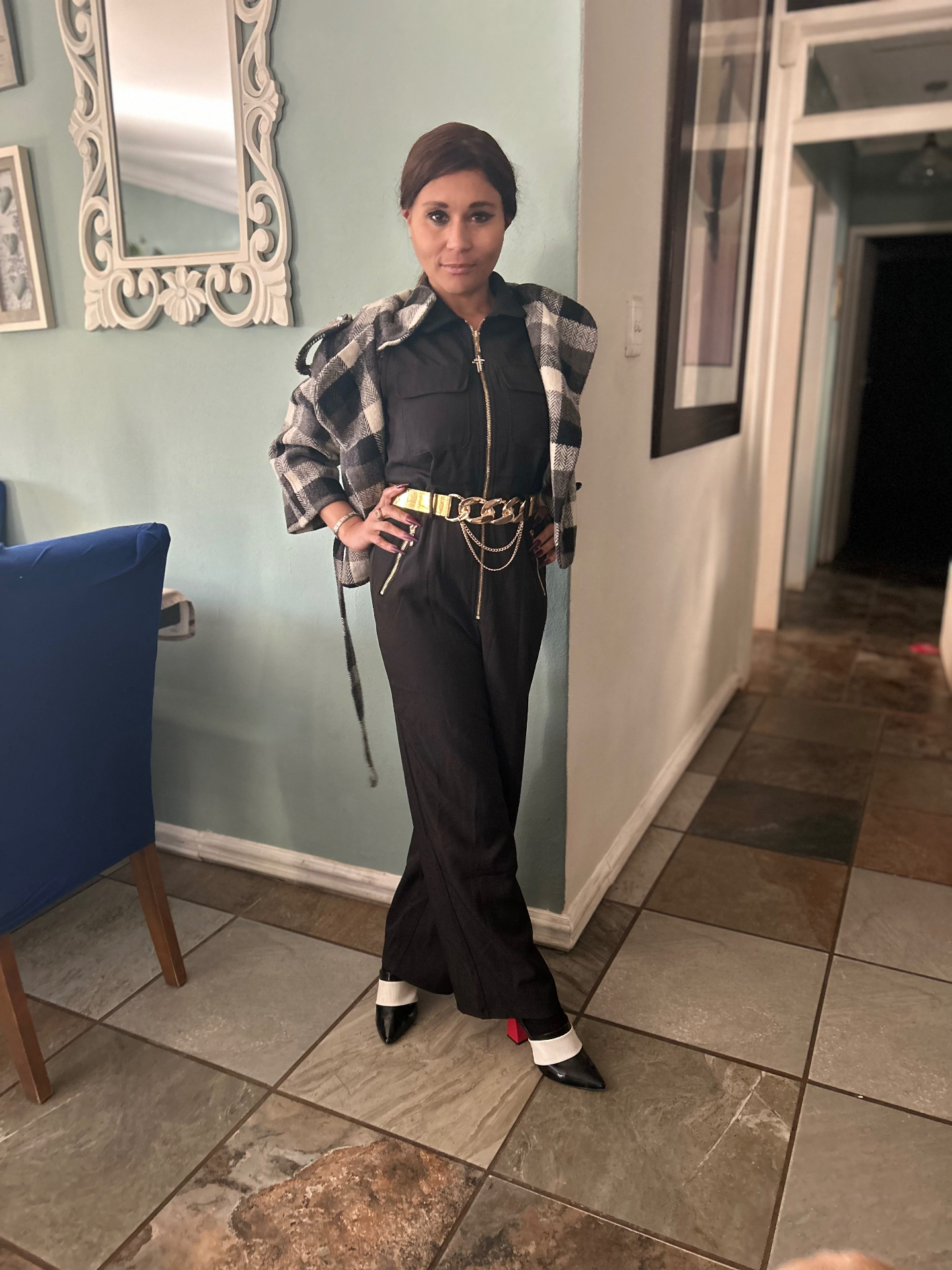Cass wearing the black jumpsuit with a black, white and grey buffalo-check shacket draped over the shoulders