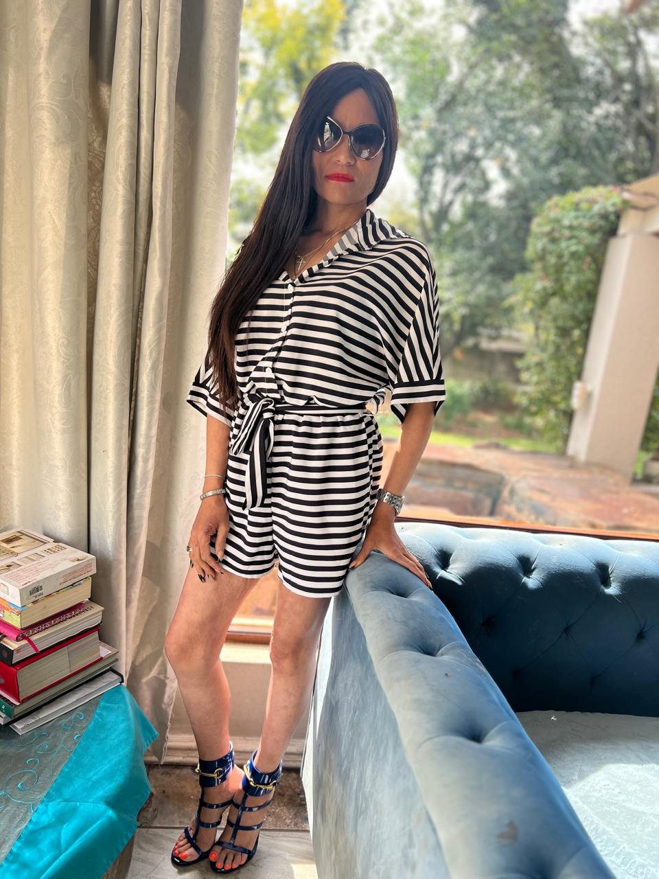 Cass in a black-and-white striped romper with navy strappy heels, gold sunglasses and a red lip — head-to-toe styling against a Tiffany blue tufted sofa