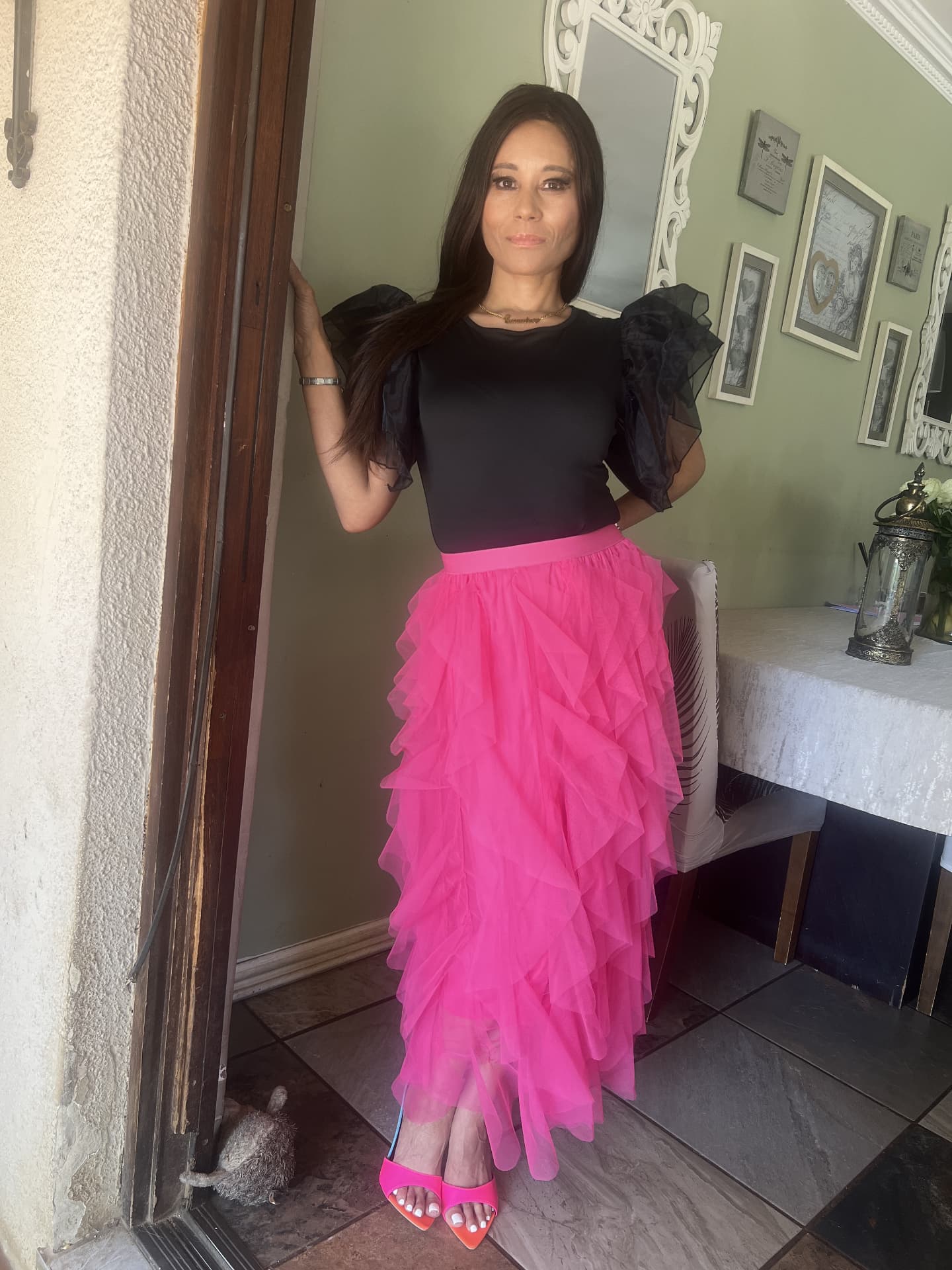 Cass in a black organza-sleeve bodysuit and hot-pink tiered tulle skirt with pink mules, standing in a doorway