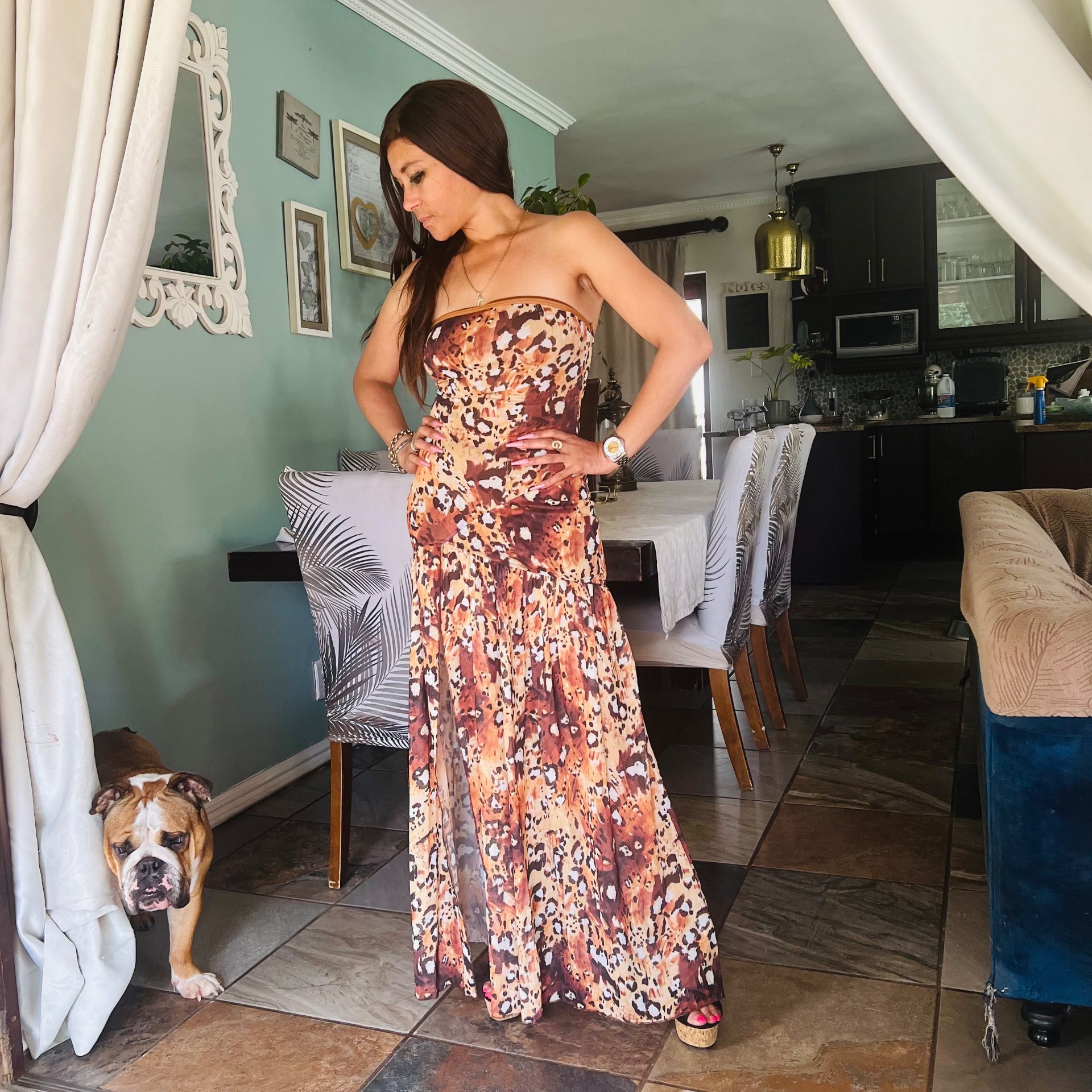 Cass in the leopard-print maxi dress looking down, with an English bulldog peeking from behind a curtain